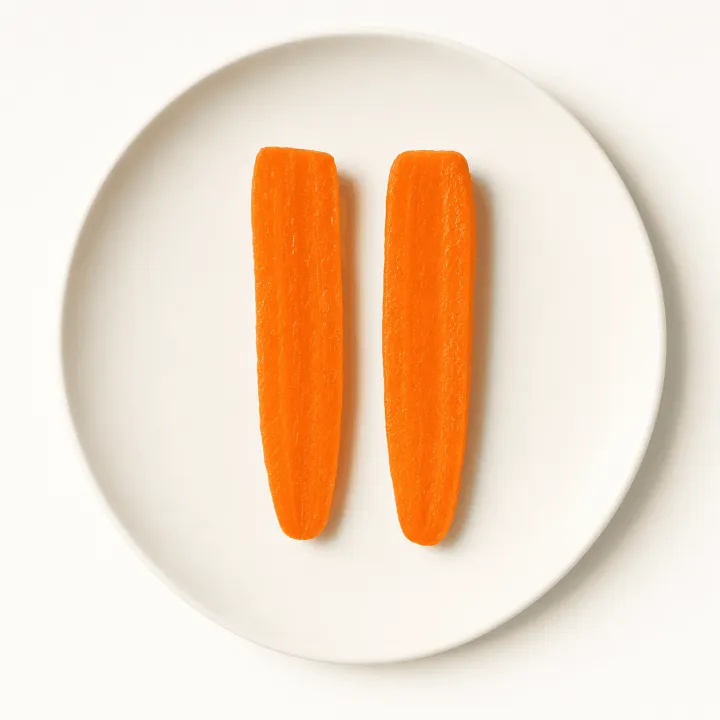 Due bastoncini di carota ben cotti su un piatto bianco, fotografati dall’alto.